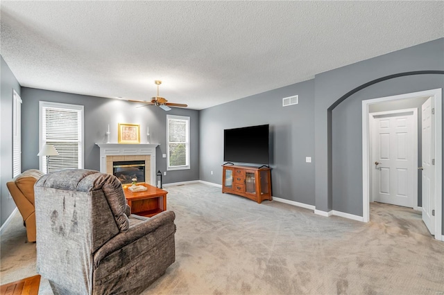 living area with baseboards, visible vents, arched walkways, a tiled fireplace, and light colored carpet