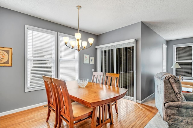 dining room featuring baseboards, light wood finished floors, a textured ceiling, and an inviting chandelier