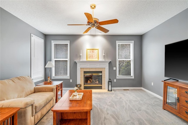 carpeted living area featuring a textured ceiling, ceiling fan, a fireplace, and baseboards