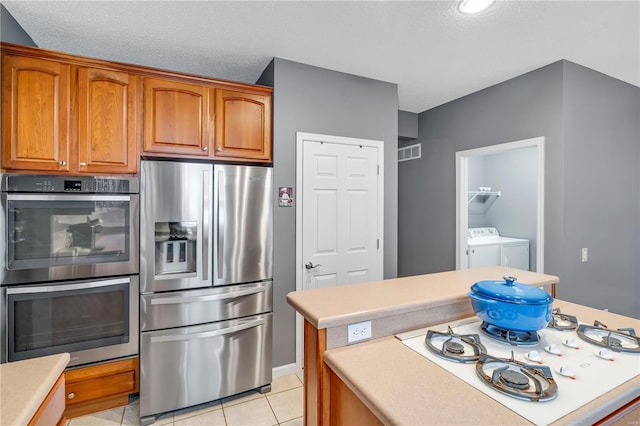 kitchen with light tile patterned floors, visible vents, stainless steel appliances, washer and dryer, and light countertops