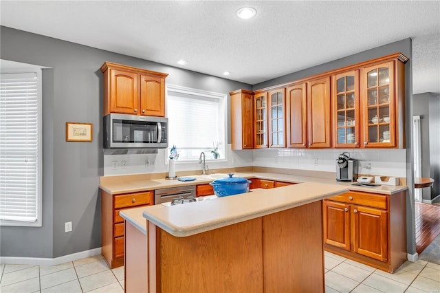 kitchen featuring a center island, light countertops, appliances with stainless steel finishes, glass insert cabinets, and light tile patterned flooring