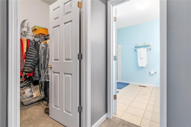 hallway featuring light tile patterned flooring, baseboards, visible vents, and light colored carpet