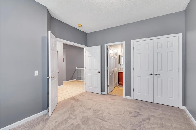 unfurnished bedroom featuring light carpet, baseboards, connected bathroom, a textured ceiling, and a closet