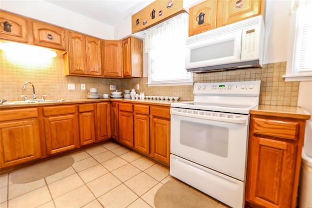 kitchen with brown cabinetry, white appliances, light countertops, and a sink