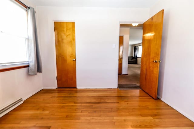 unfurnished room featuring a baseboard heating unit, baseboards, plenty of natural light, and light wood finished floors