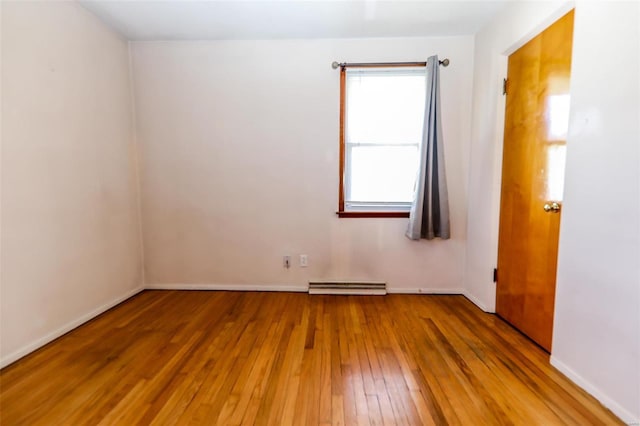 unfurnished room featuring wood-type flooring, a baseboard heating unit, and baseboards