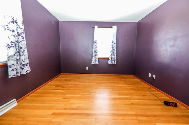 unfurnished room with a baseboard heating unit, wood finished floors, and baseboards