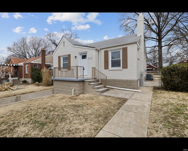 bungalow-style home featuring brick siding, fence, a gate, a front lawn, and a chimney