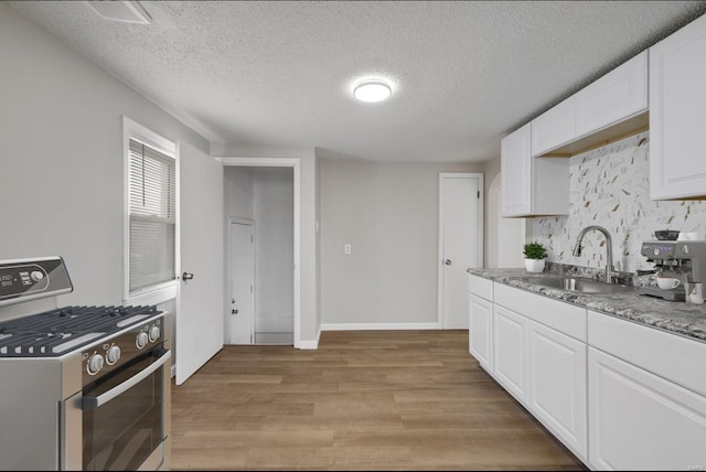 kitchen featuring gas range, light wood-style flooring, a sink, white cabinetry, and backsplash