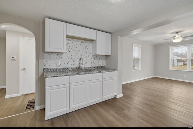 kitchen featuring arched walkways, tasteful backsplash, white cabinets, a sink, and wood finished floors