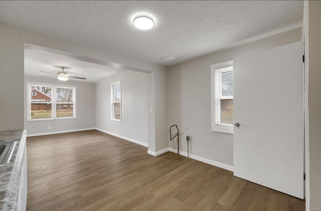 unfurnished living room with ceiling fan, a textured ceiling, baseboards, and wood finished floors