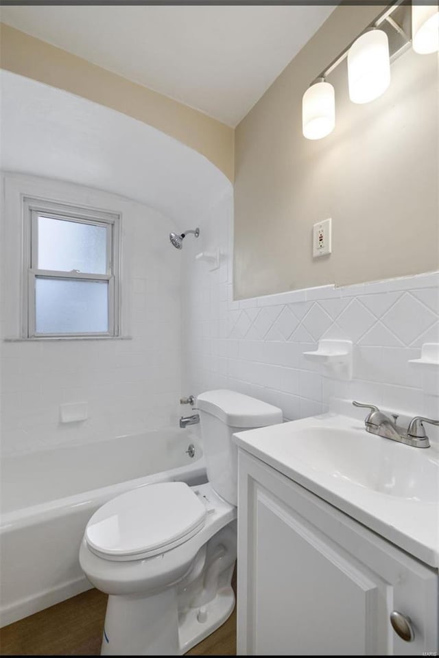 full bath featuring toilet, vanity, tile walls, shower / washtub combination, and wainscoting