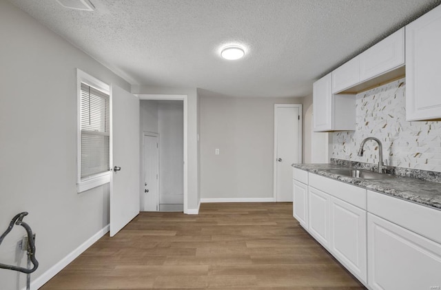 kitchen with a sink, baseboards, white cabinets, light wood-style floors, and decorative backsplash