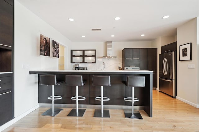 kitchen with wall chimney range hood, modern cabinets, a breakfast bar, and freestanding refrigerator