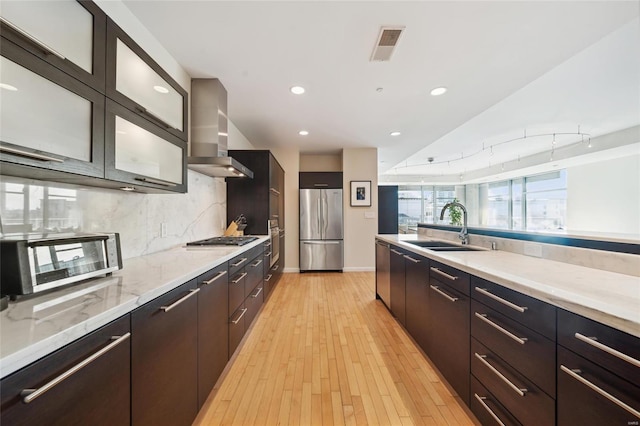 kitchen with stainless steel appliances, glass insert cabinets, a sink, modern cabinets, and wall chimney exhaust hood