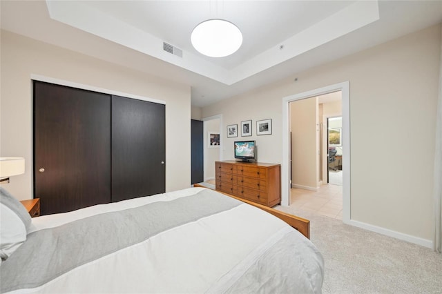 bedroom featuring a closet, light colored carpet, a raised ceiling, visible vents, and baseboards