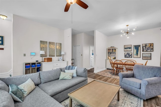 living room featuring ceiling fan with notable chandelier, baseboards, and wood finished floors