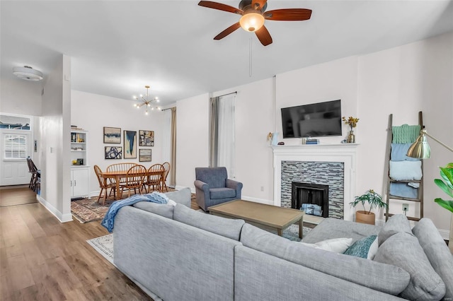 living area featuring baseboards, ceiling fan with notable chandelier, wood finished floors, and a tile fireplace