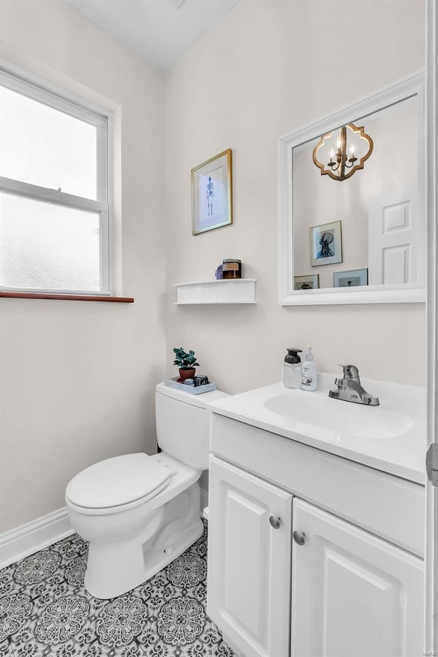 half bathroom with vanity, baseboards, toilet, tile patterned floors, and a notable chandelier