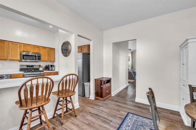 kitchen featuring baseboards, light wood finished floors, stainless steel appliances, light countertops, and a kitchen bar