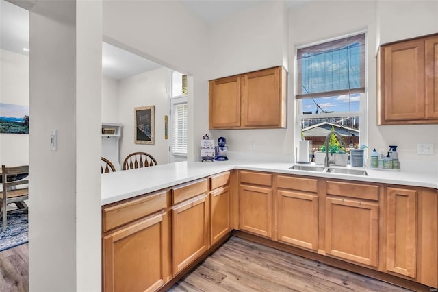 kitchen featuring a sink, light wood-style floors, a peninsula, and light countertops