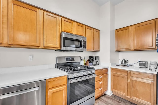 kitchen with light wood-type flooring, stainless steel appliances, and light countertops