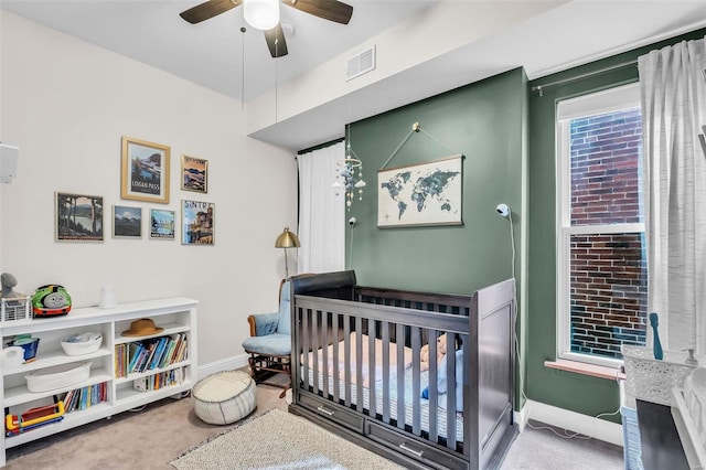 carpeted bedroom with a crib, baseboards, visible vents, and a ceiling fan