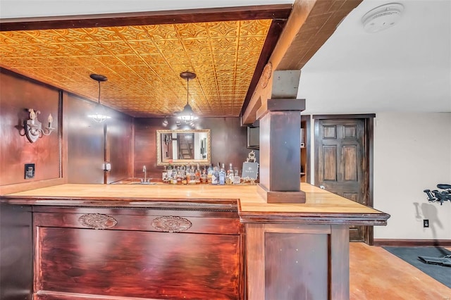 bar featuring baseboards, decorative light fixtures, indoor wet bar, an ornate ceiling, and a sink