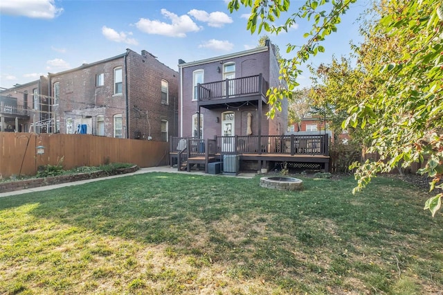 rear view of property featuring an outdoor fire pit, a wooden deck, a yard, and fence