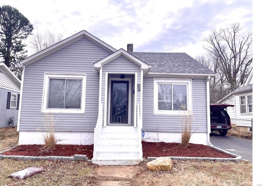 bungalow featuring driveway, a chimney, and roof with shingles