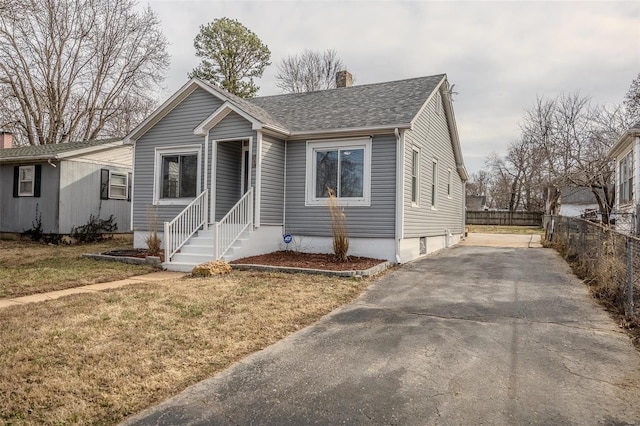 bungalow-style home featuring a shingled roof, a chimney, a front lawn, and fence