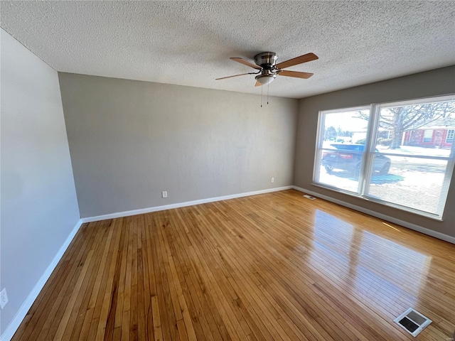 empty room with visible vents, light wood-type flooring, a ceiling fan, and baseboards