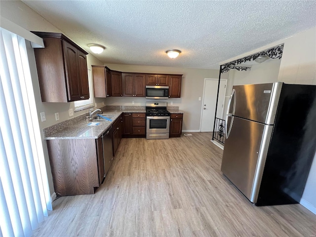 kitchen with stainless steel appliances, light wood-style floors, a textured ceiling, and a sink