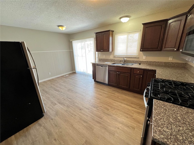 kitchen with appliances with stainless steel finishes, a sink, dark brown cabinetry, and light wood-style floors