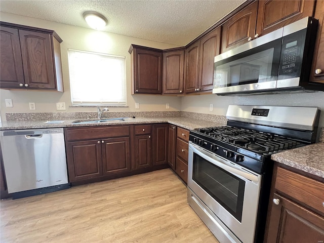 kitchen with a textured ceiling, appliances with stainless steel finishes, a sink, and light wood-style floors