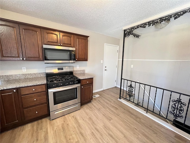 kitchen with visible vents, stainless steel appliances, dark brown cabinets, a textured ceiling, and light wood-style floors