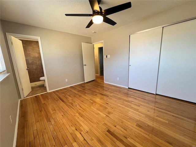 unfurnished bedroom featuring a textured ceiling, ensuite bathroom, baseboards, light wood-style floors, and a closet