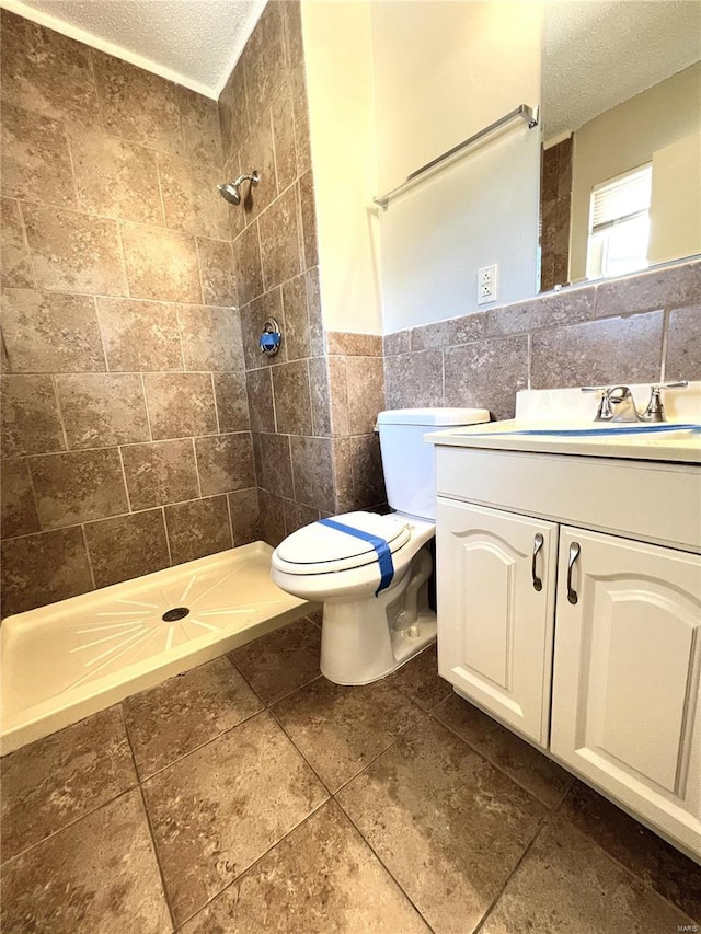 bathroom with tile walls, wainscoting, a tile shower, a textured ceiling, and vanity