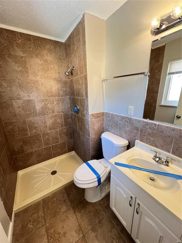 bathroom with wainscoting, a tile shower, a textured ceiling, vanity, and tile walls