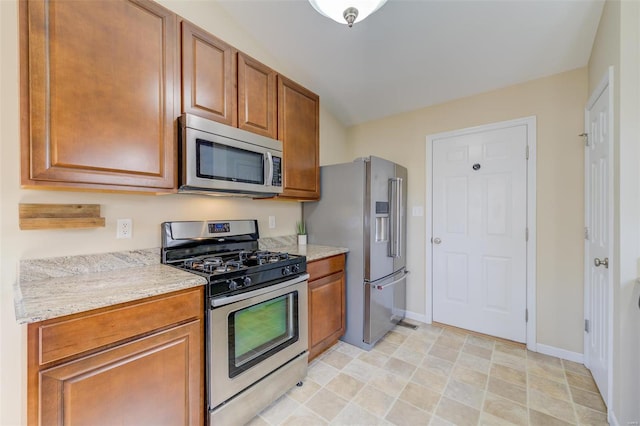 kitchen with light stone counters, brown cabinetry, baseboards, and appliances with stainless steel finishes