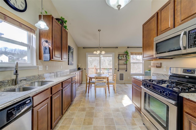 kitchen with light stone countertops, brown cabinetry, a sink, hanging light fixtures, and appliances with stainless steel finishes