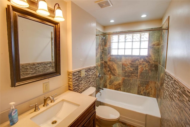 bathroom featuring visible vents, wainscoting, toilet, shower / washtub combination, and tile walls