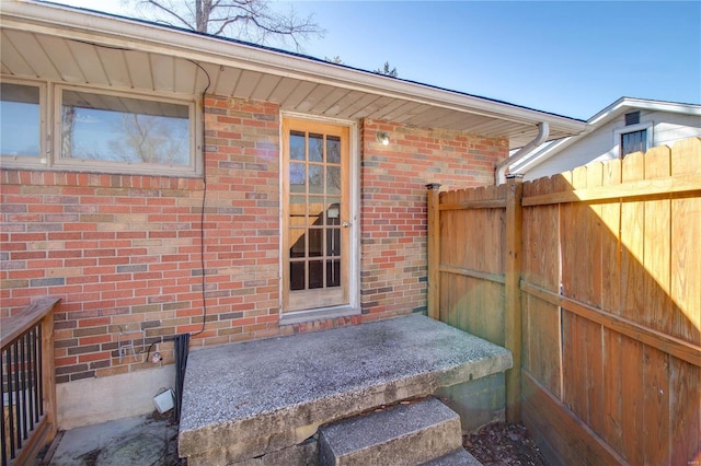 doorway to property with brick siding and fence