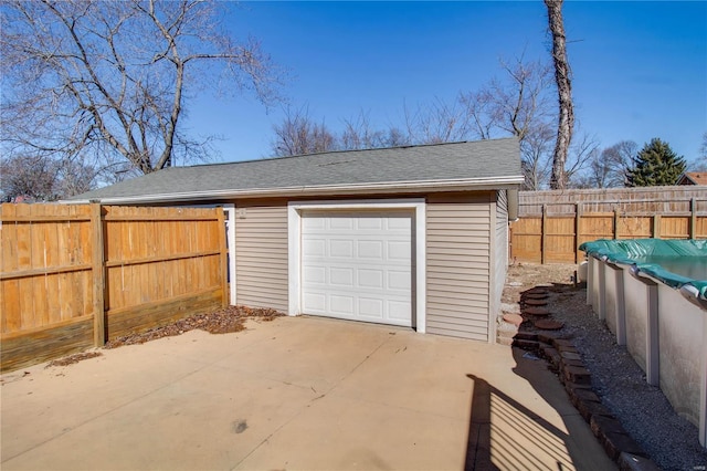 garage with concrete driveway, fence, and a fenced in pool