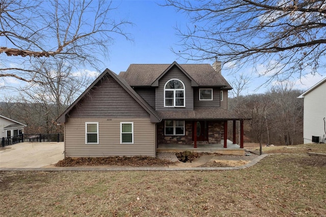 view of front facade featuring covered porch, stone siding, roof with shingles, a chimney, and a front yard