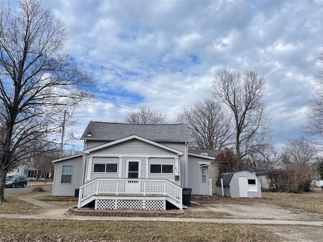 bungalow with dirt driveway, a shingled roof, a storage shed, an outdoor structure, and a wooden deck