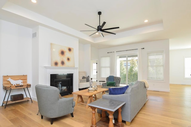 living room with light wood finished floors, visible vents, baseboards, a glass covered fireplace, and a tray ceiling