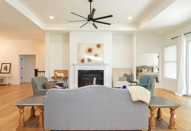 living area featuring recessed lighting, light wood-style flooring, a tray ceiling, and a glass covered fireplace