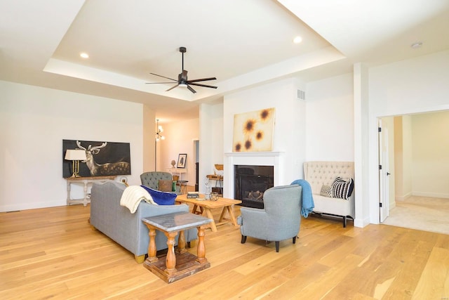 living area with baseboards, a tray ceiling, a glass covered fireplace, and light wood-style floors