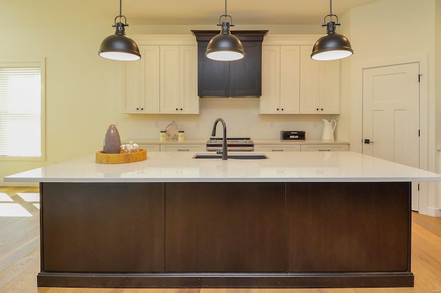 kitchen with light wood finished floors, a kitchen island with sink, white cabinetry, and a sink